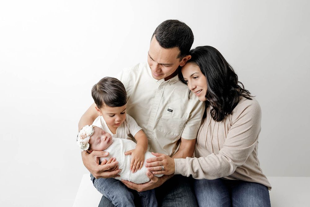 Loving family of four gazing at swaddled newborn baby during professional studio portrait session.