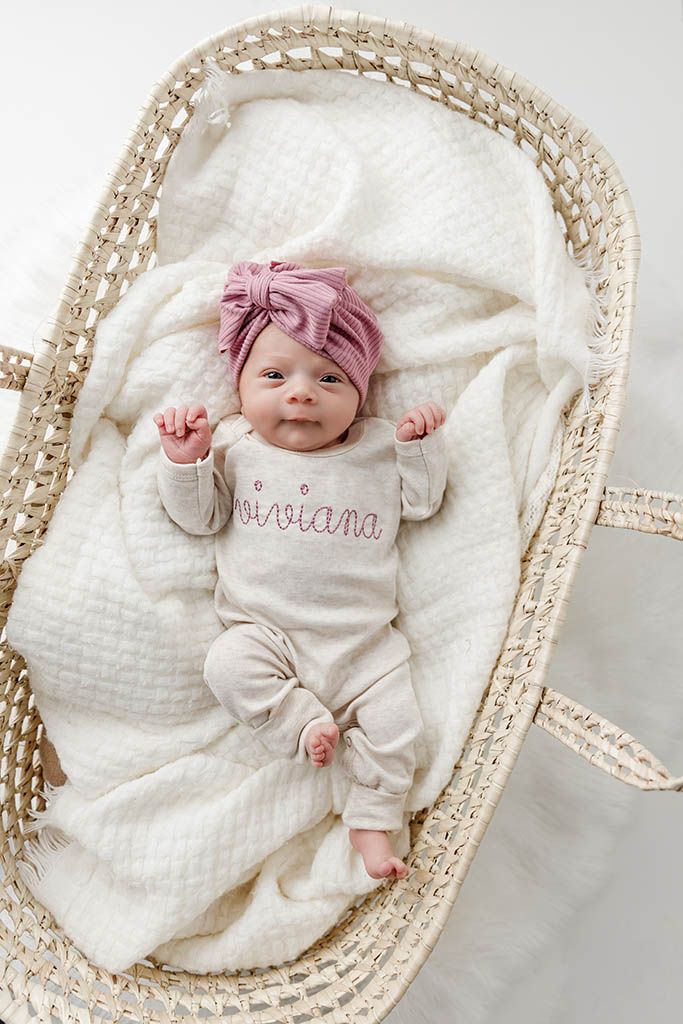 Newborn baby girl named Viviana in personalized onesie and pink turban bow in wicker moses basket.