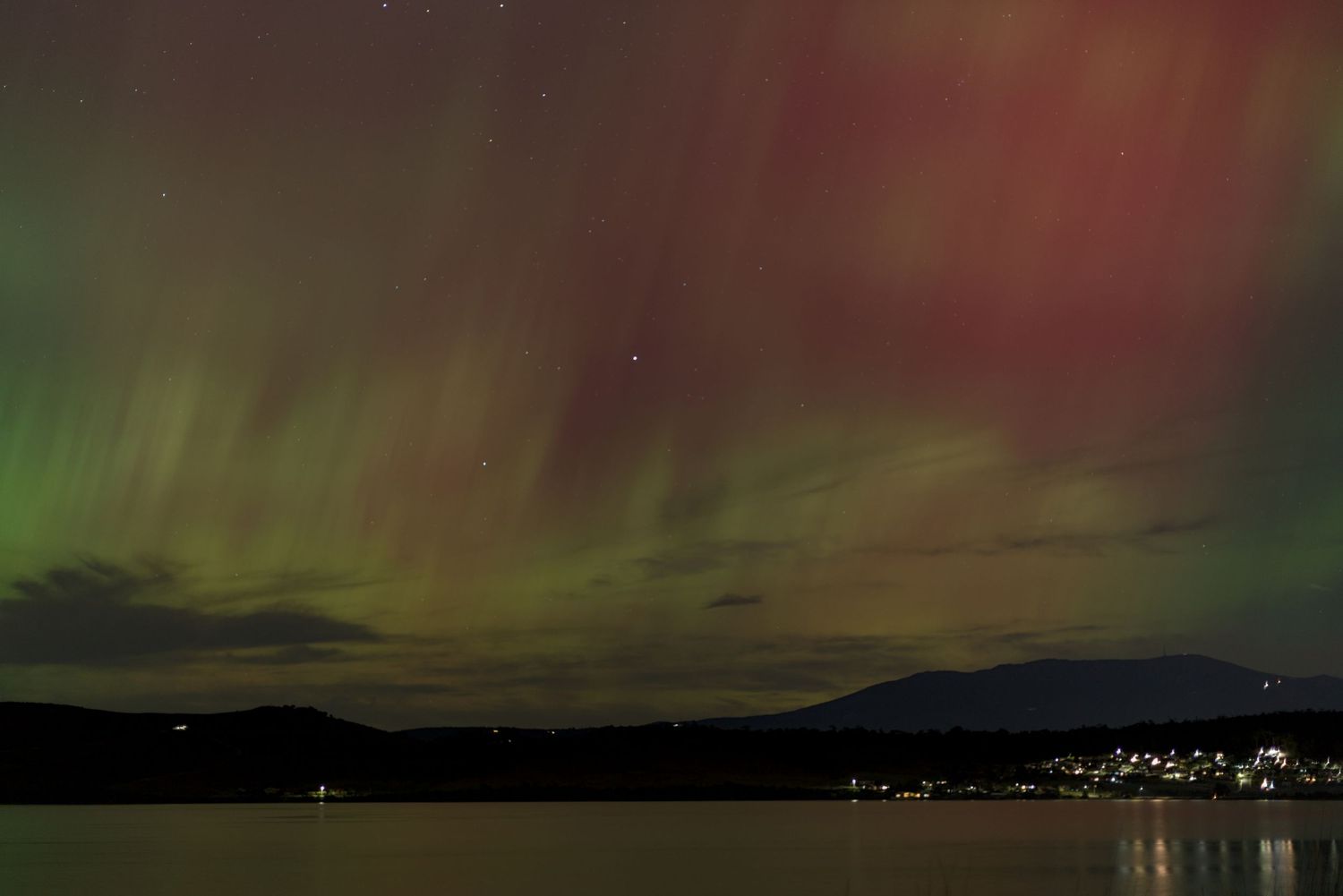 Aurora australis casting green and purple hues over a historic stone arch bridge at night.