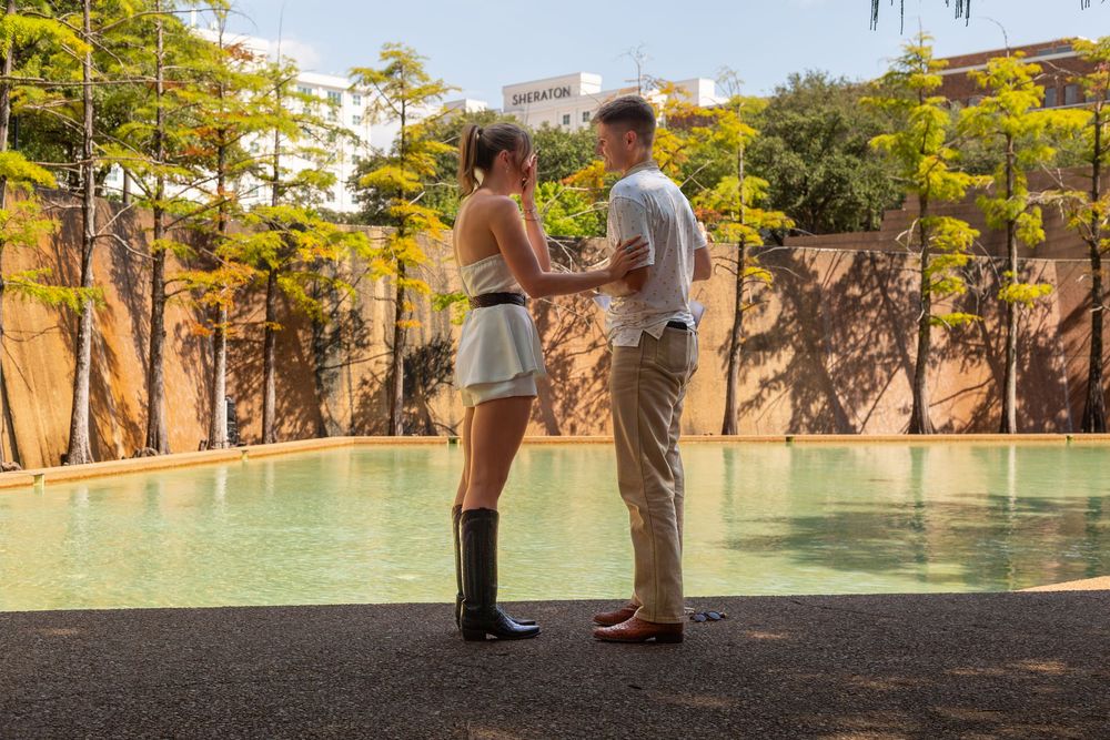 Couple holding hands by a serene pool surrounded by lush trees at a tropical resort.