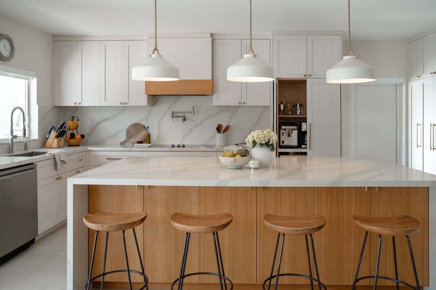 Bright modern kitchen with marble island, wood barstools, pendant lights, and white cabinetry with marble backsplash.