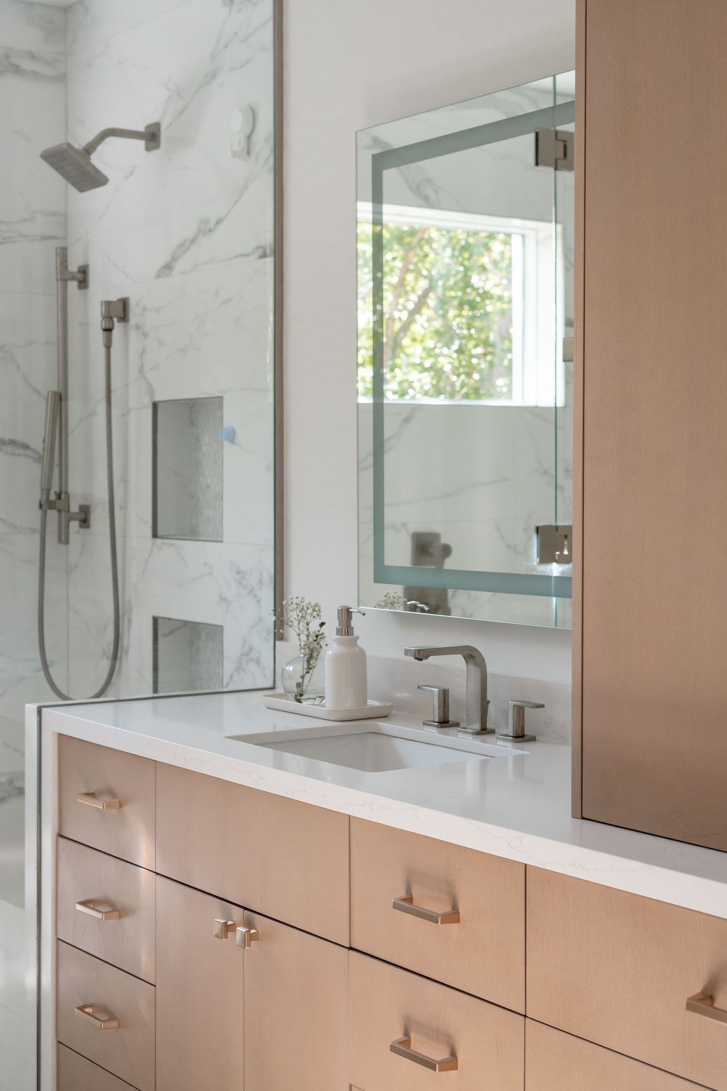 Modern bathroom with marble walls, light wood vanity, white quartz countertop, undermount sink, and brushed nickel fixtures.