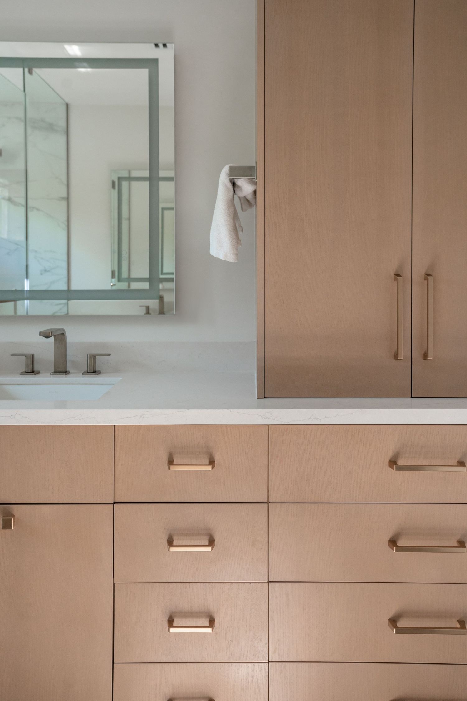 Modern bathroom vanity with light wood cabinets, brushed nickel hardware, white countertop, undermount sink, and framed mirror.