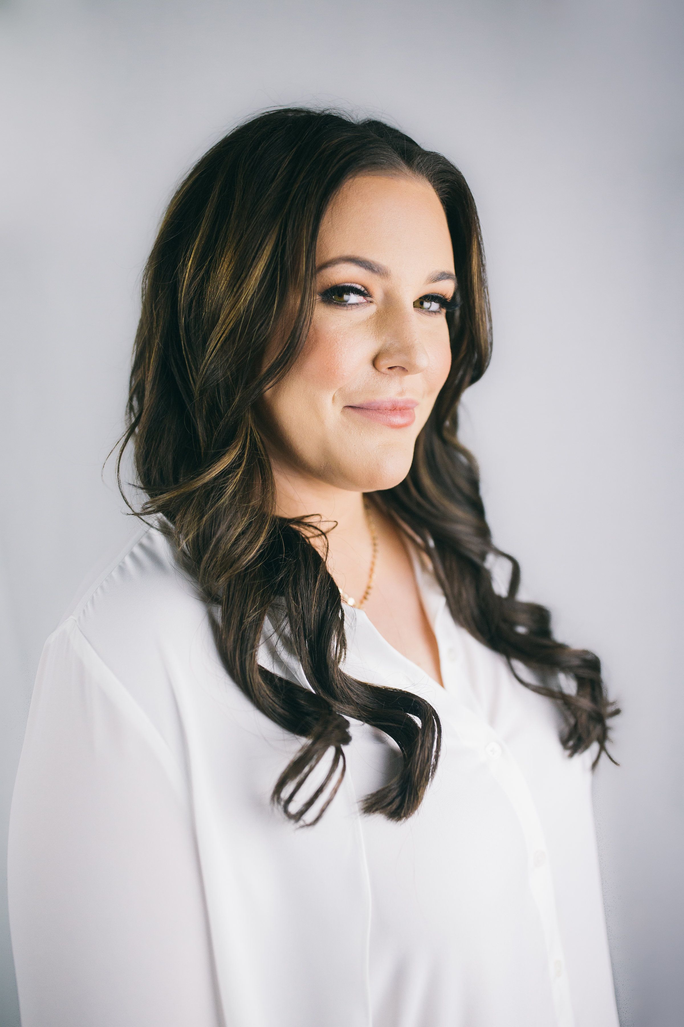 headshot of Caroline Kraddick wearing a white shirt on a white background, smirking and looking from the side, long hair