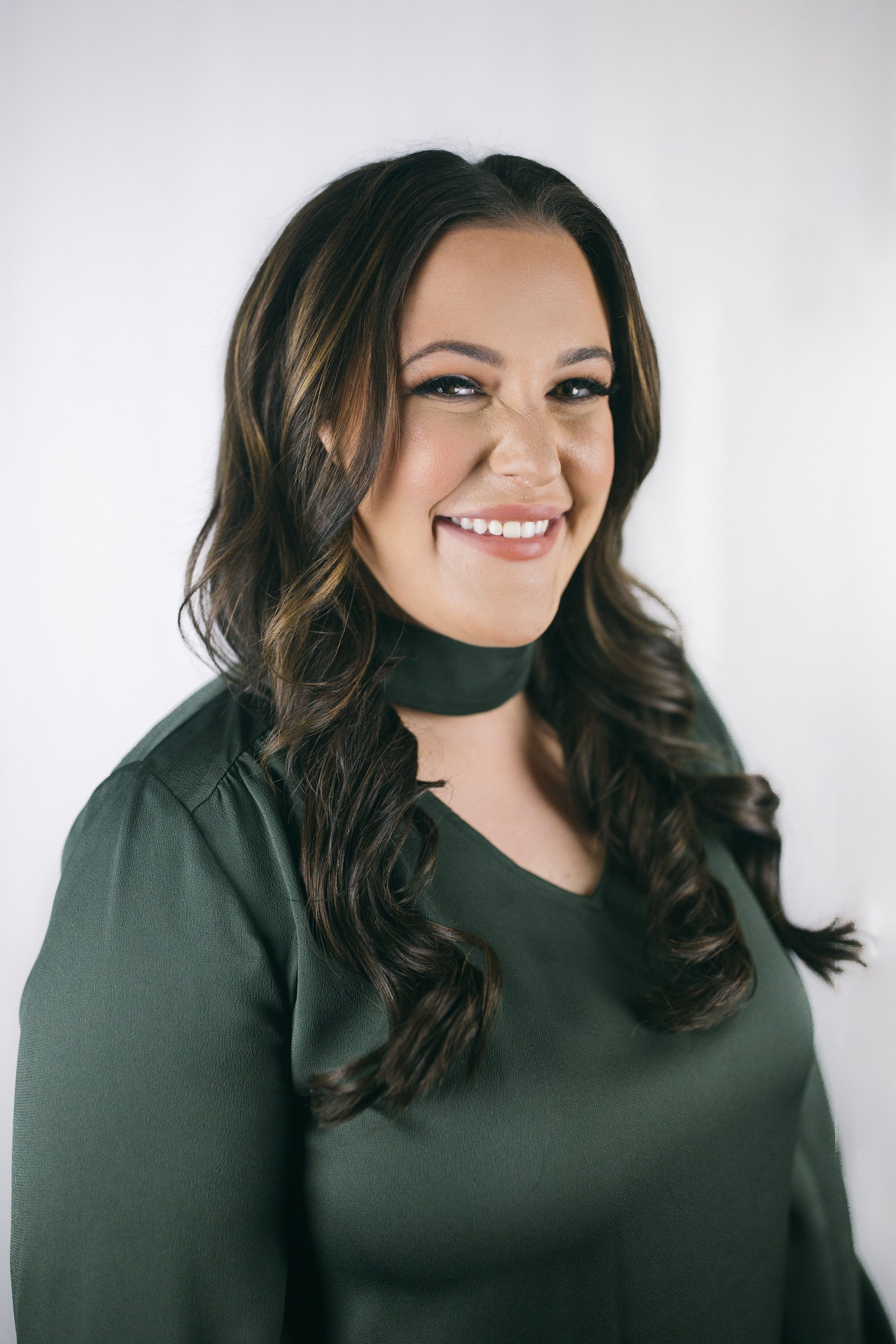 headshot of Caroline Kraddick in green silk shirt with a big smile, scrunched nose and long curled hair