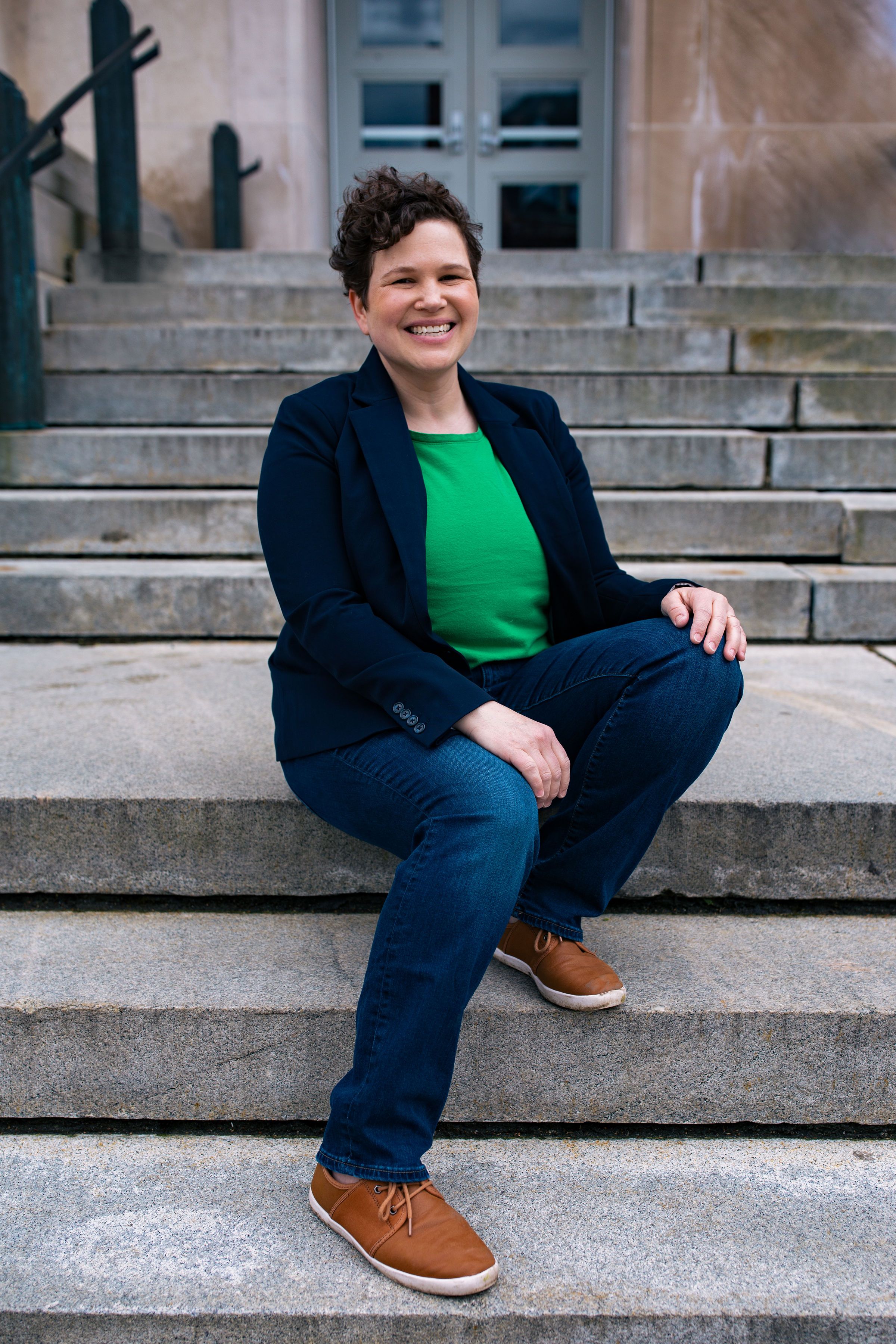sitting portrait of smiling queer woman, on cement steps, in Malden, MA