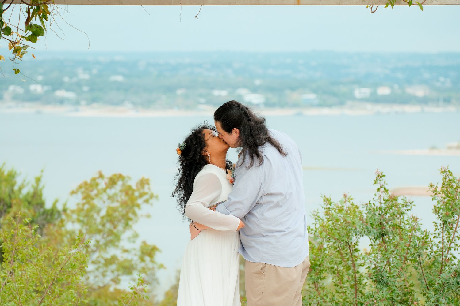 Couple sharing a romantic kiss with a scenic lake and blue sky in the background.