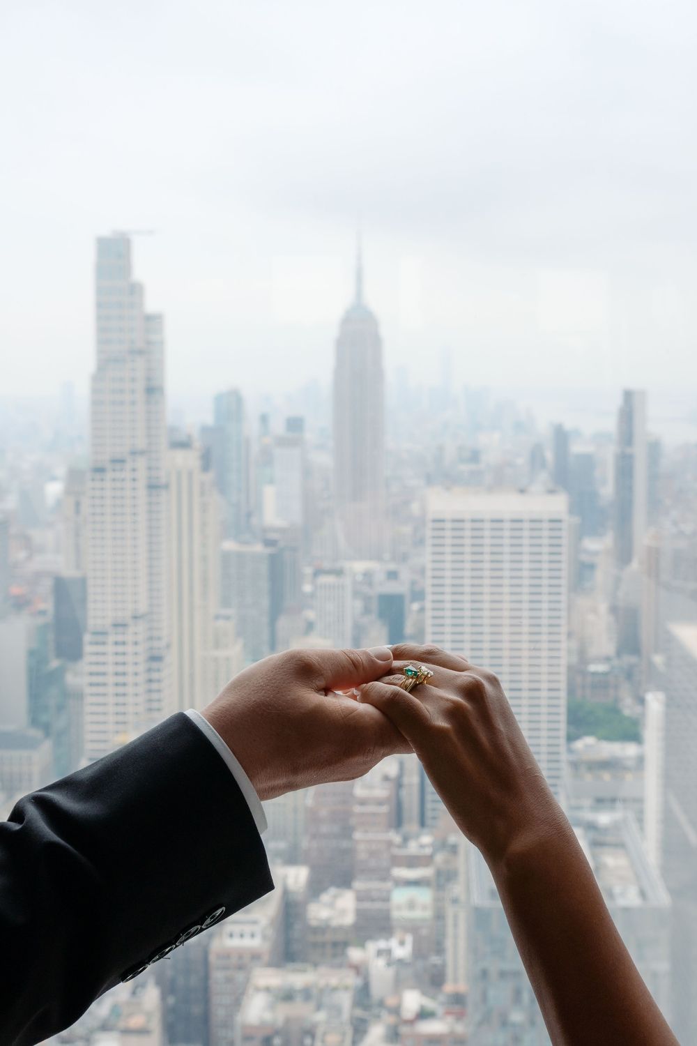 Couple holding hands with engagement ring overlooking New York City skyline and Empire State Building.