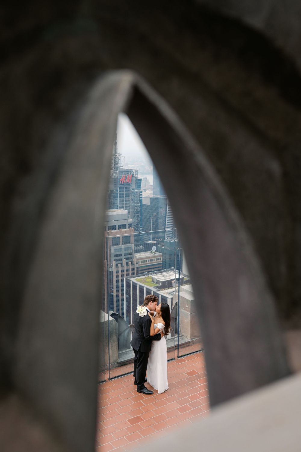 Couple sharing a romantic kiss framed through a sculptural arch, with a stunning city skyline backdrop.