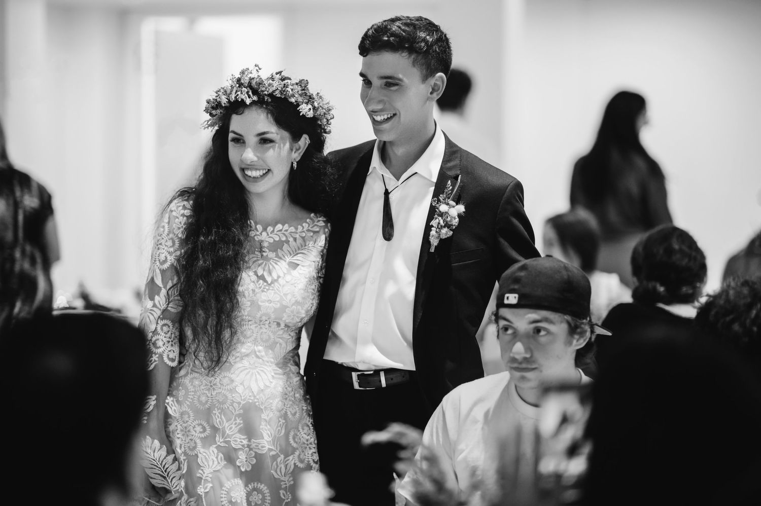 Black and white wedding photo of smiling bride with floral crown and groom in suit at elegant reception.