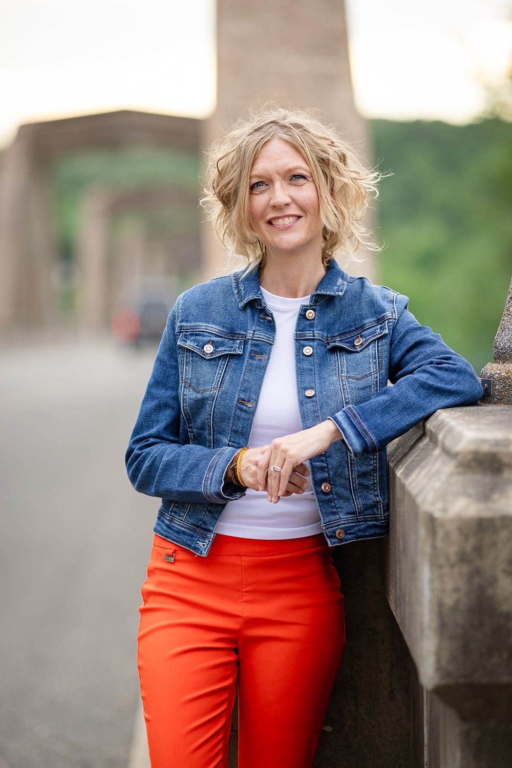 Realtor in a denim jacket leaning on the Cotter Bridge railing for a personal branding photo in Cotter, Arkansas