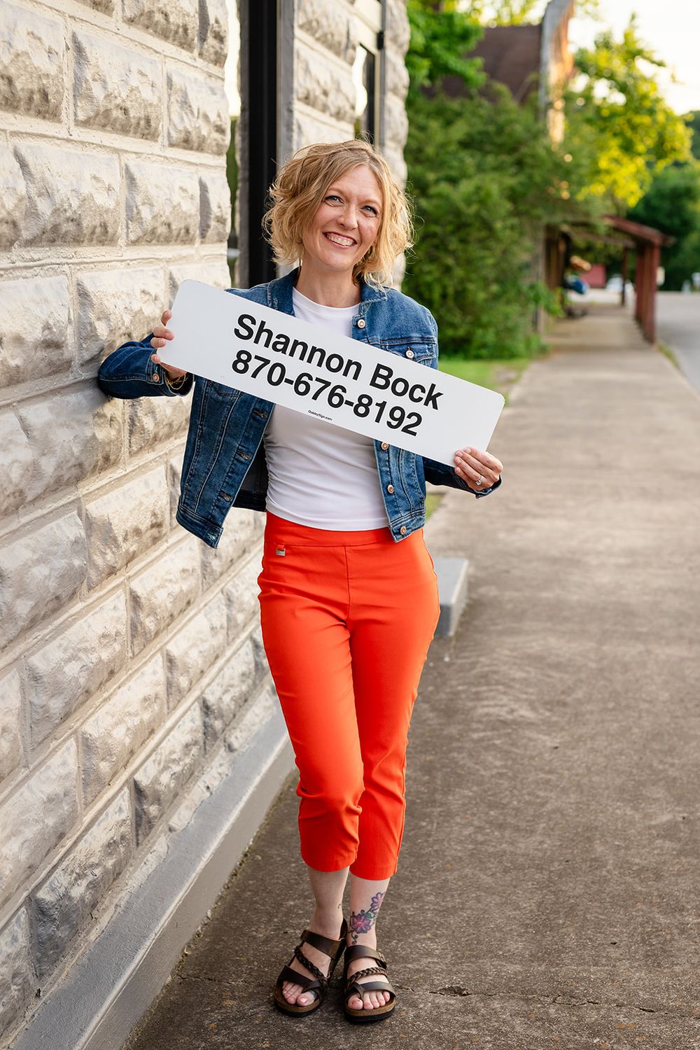 Personal branding photo of a real estate agent holding her name sign by a brick wall in Cotter, Arkansas