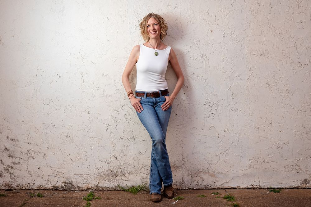 Realtor leaning against a white wall for a personal branding photo in Cotter, Arkansas