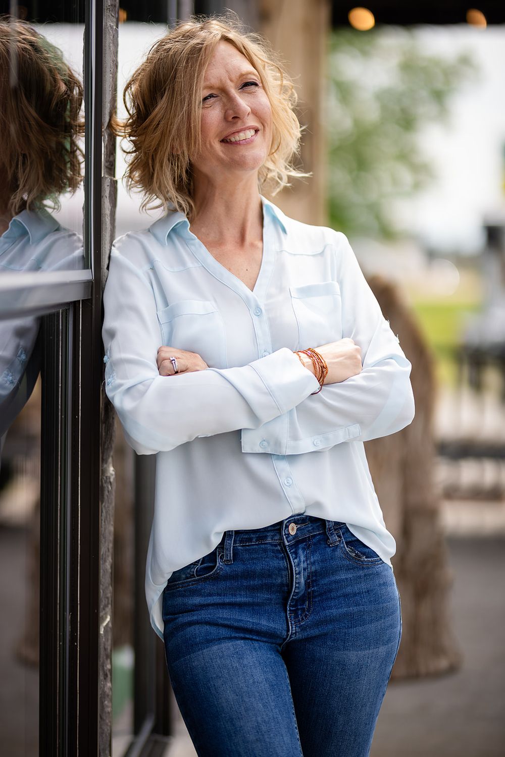 Realtor with arms crossed leaning by a storefront window for a personal branding session in Gassville, Arkansas
