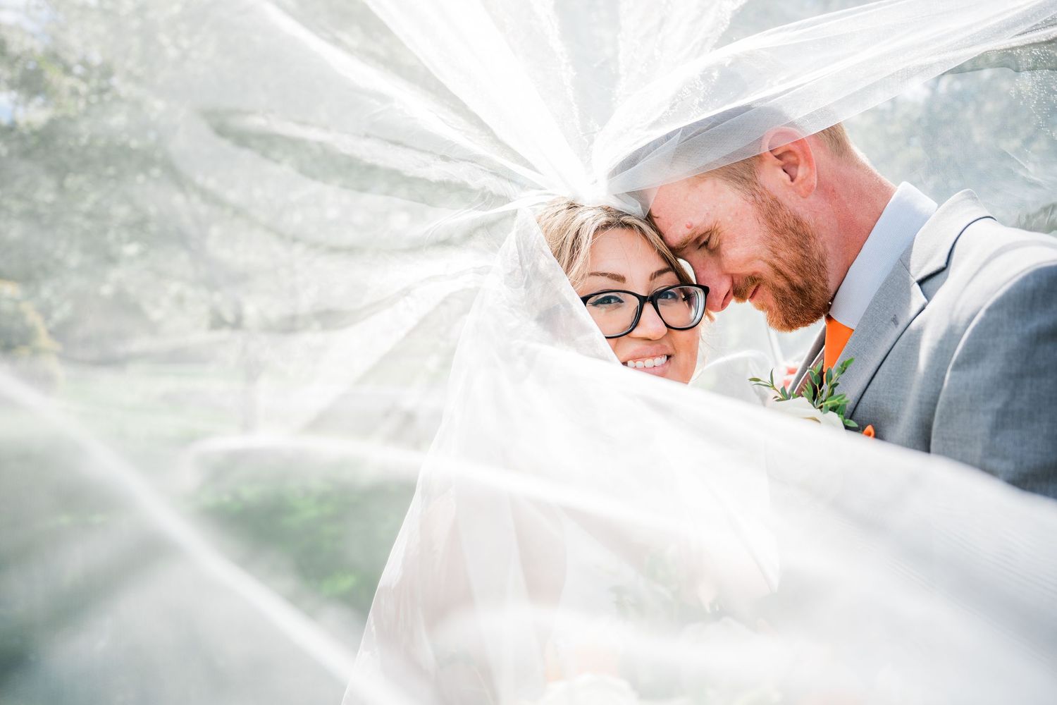 Bride and groom smiling under white wedding veil, bride and groom in gray suit with floral boutonniere at Wood Acres Farm Terryville CT