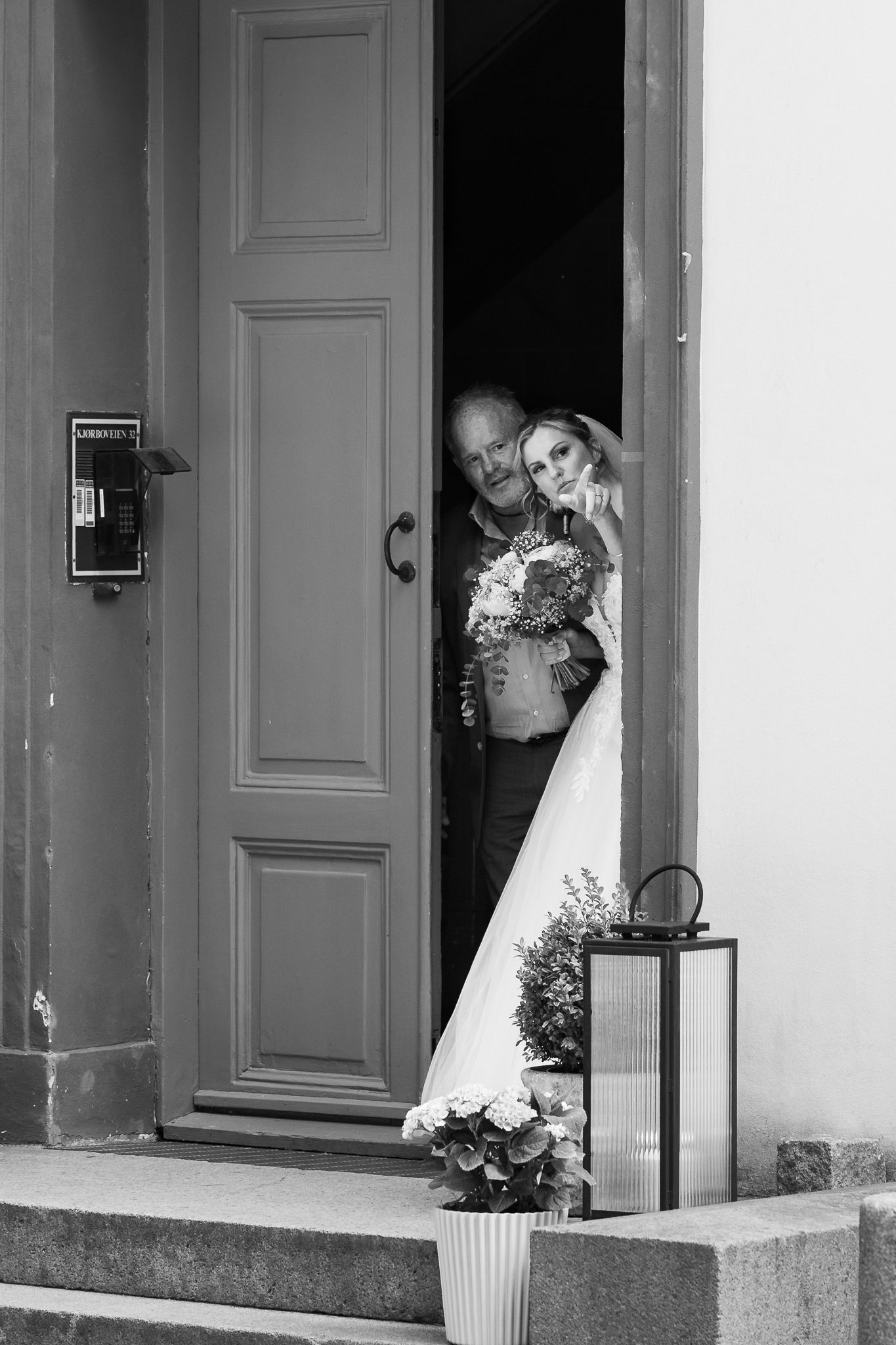 Black and white photo of a bride and groom peeking through an open church door on their wedding day.