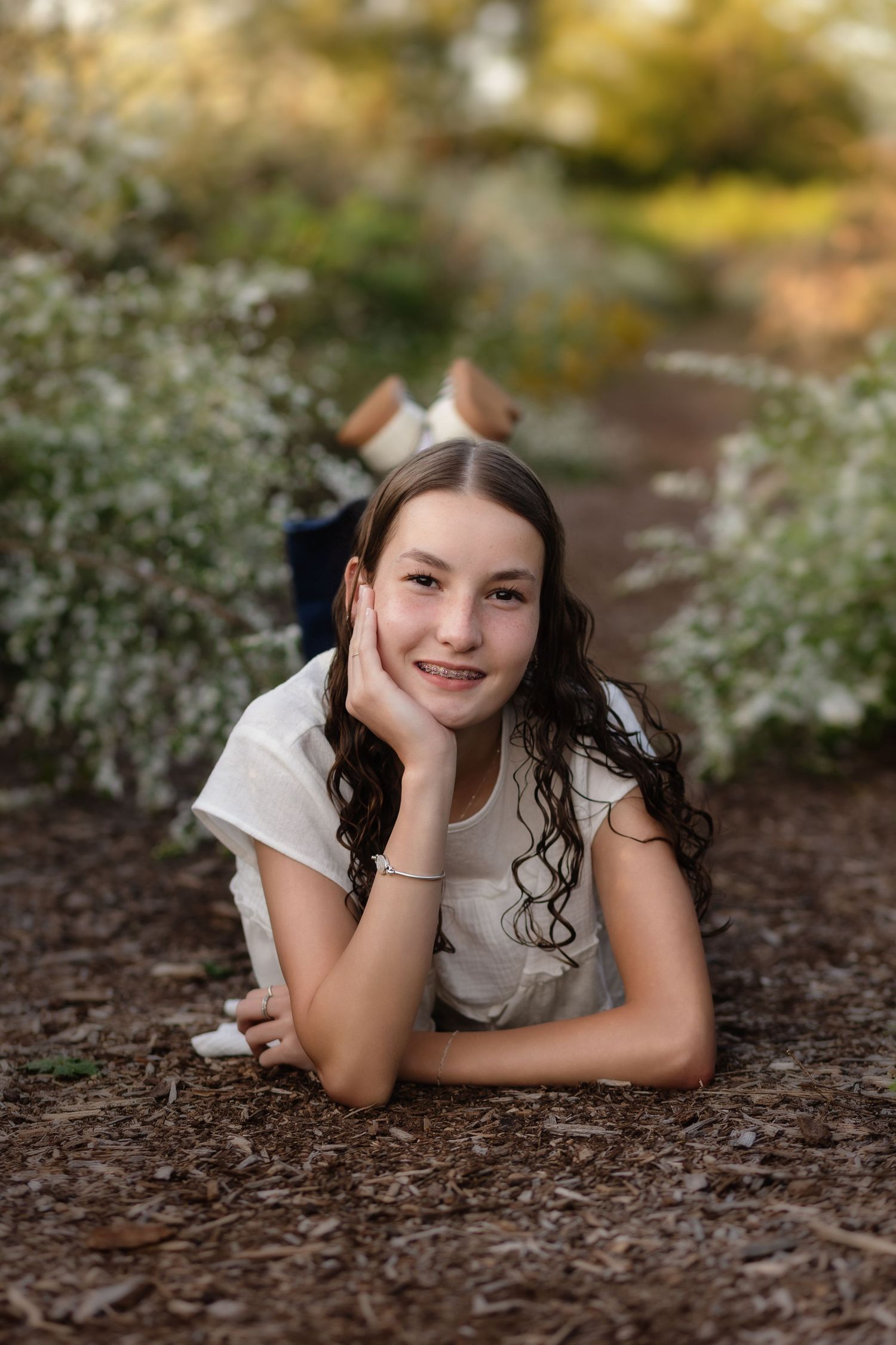 Senior girl rests on her arms on a pathway through a field of white flowers at Barboursville Vineyard, by Charlottesville photographer.