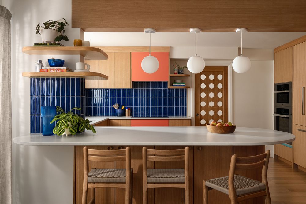 Modern kitchen with blue tile backsplash, wood cabinets, oval island, and pendant lights in a mid-century style.