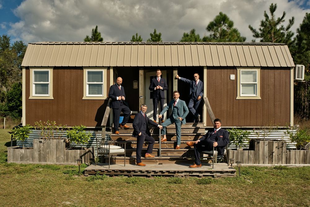 Group of groomsmen posing on rustic wooden cabin steps in suits for a wedding party photo outdoors.
