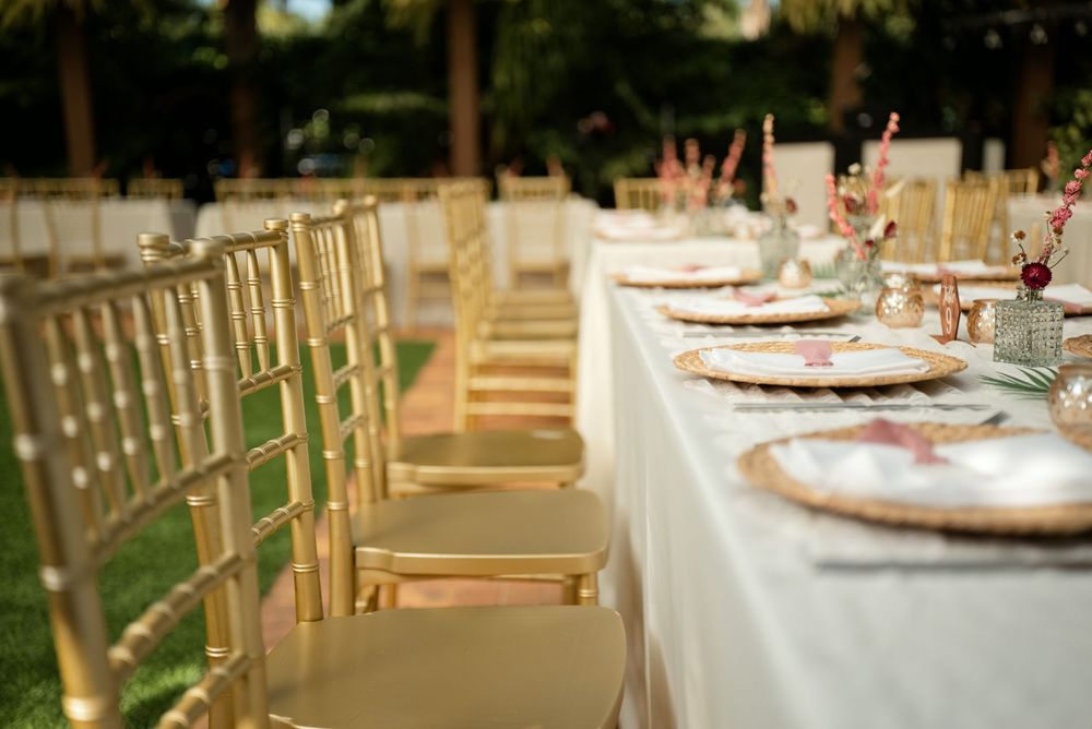 Elegant outdoor wedding reception table with gold chiavari chairs, white linen, and decorative place settings.