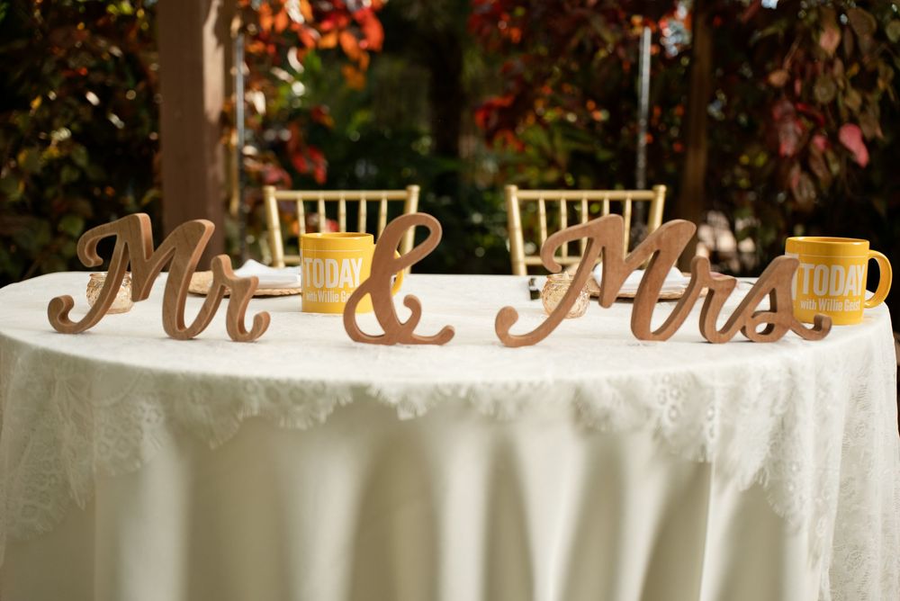Wooden Mr & Mrs signs on a white lace sweetheart table with yellow mugs at an outdoor wedding reception.