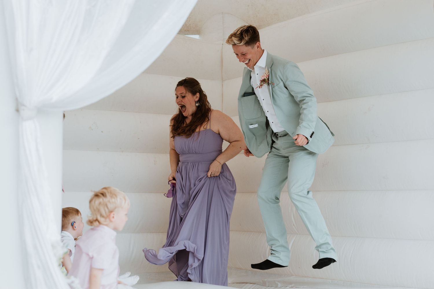 Wedding guests bouncing in a white inflatable castle with a child at a wedding reception.