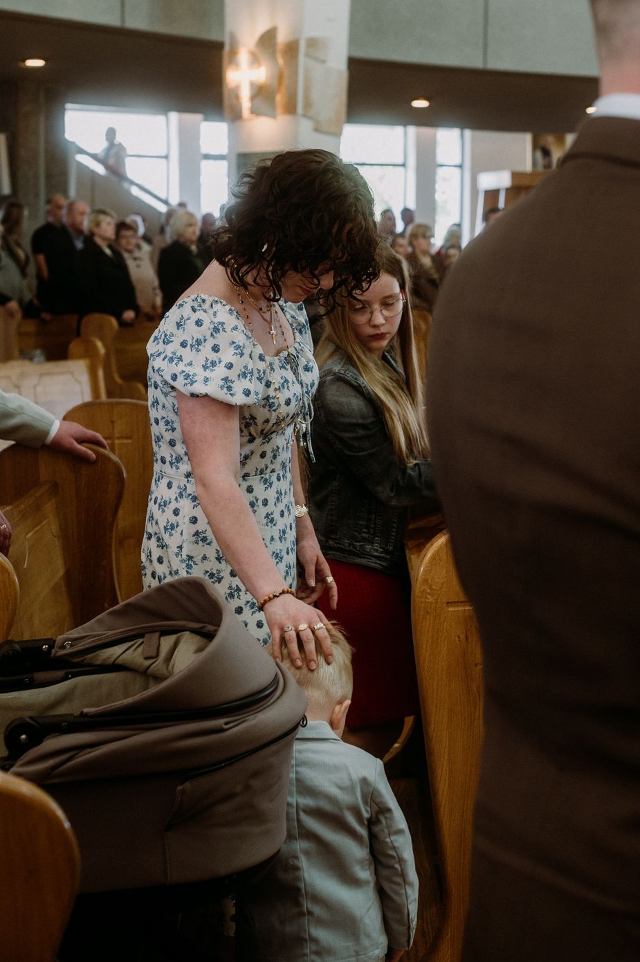 Woman in floral dress and girl in church pew during religious ceremony, gently touching child's head.