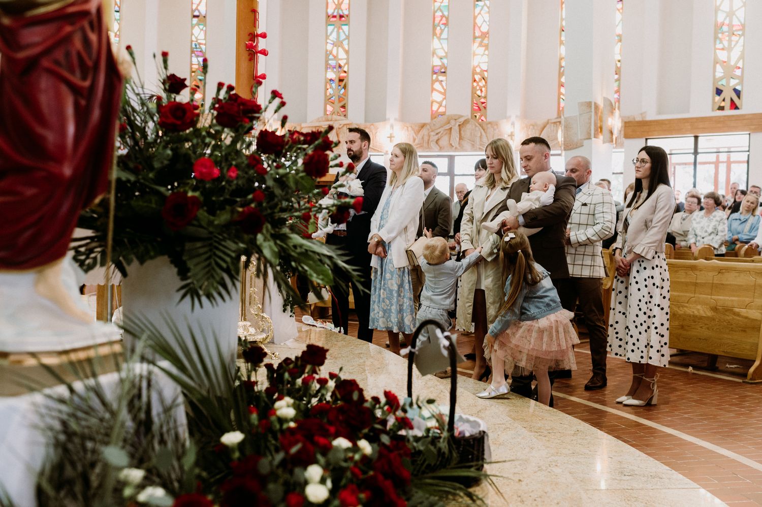 Bride and groom standing at church altar with red floral arrangements during wedding ceremony.