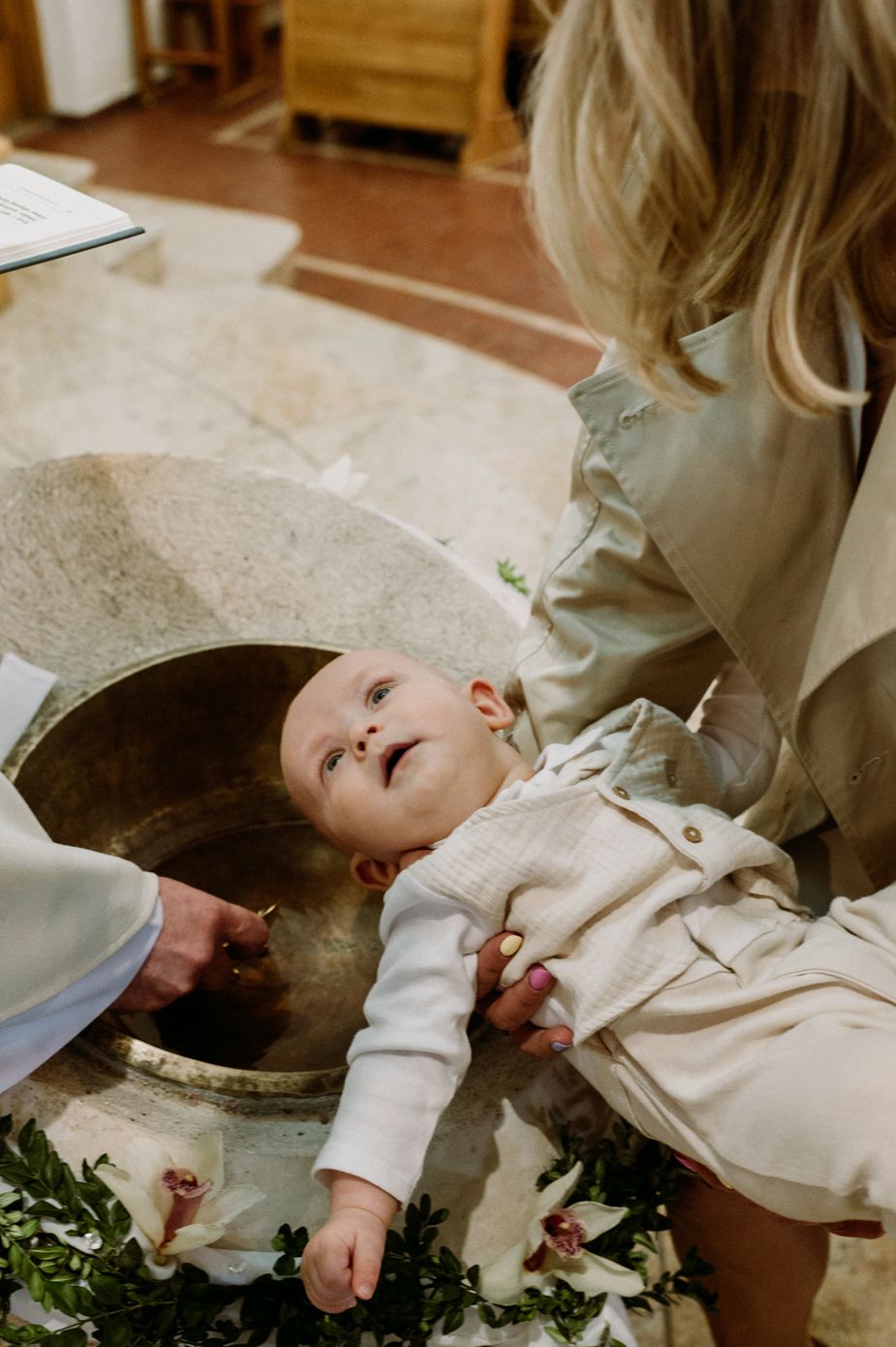 A baby being held over a baptismal font during a christening ceremony in a church.