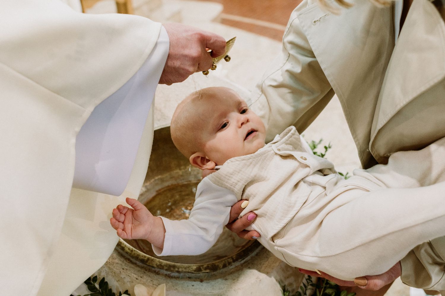 A baby being baptized in a stone font by a priest during a religious christening ceremony.
