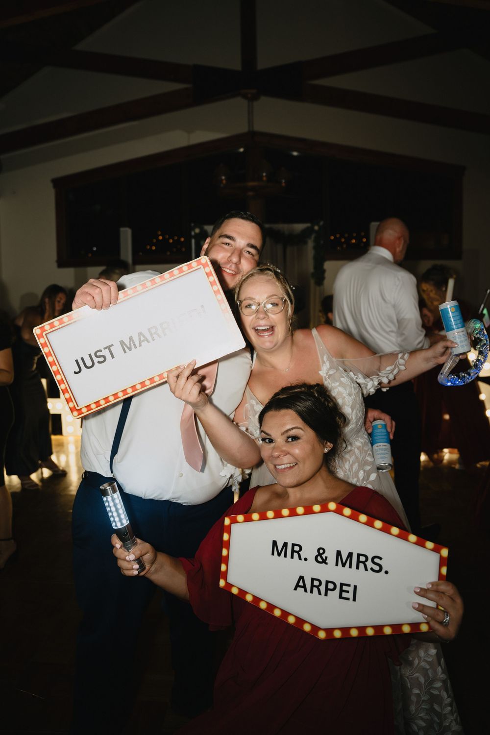 Newlyweds Mr. & Mrs. Arpei celebrate at wedding reception holding fun photo booth signs with a guest.