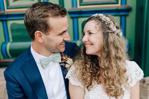 A smiling bride with curly hair and floral headpiece gazes at her groom in a blue suit with mint bow tie.