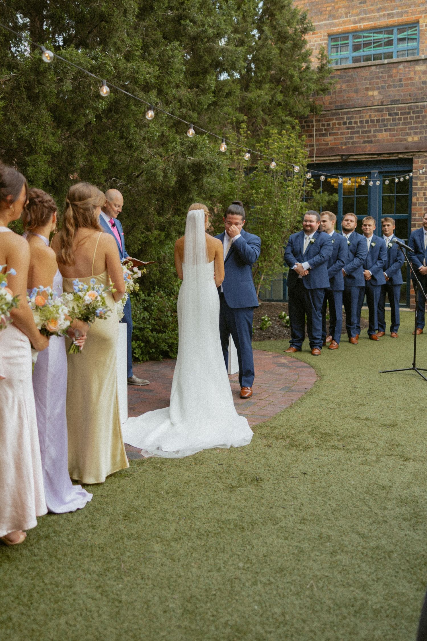 Black and white photo of bride and groom kissing under a wedding veil against a brick wall backdrop.