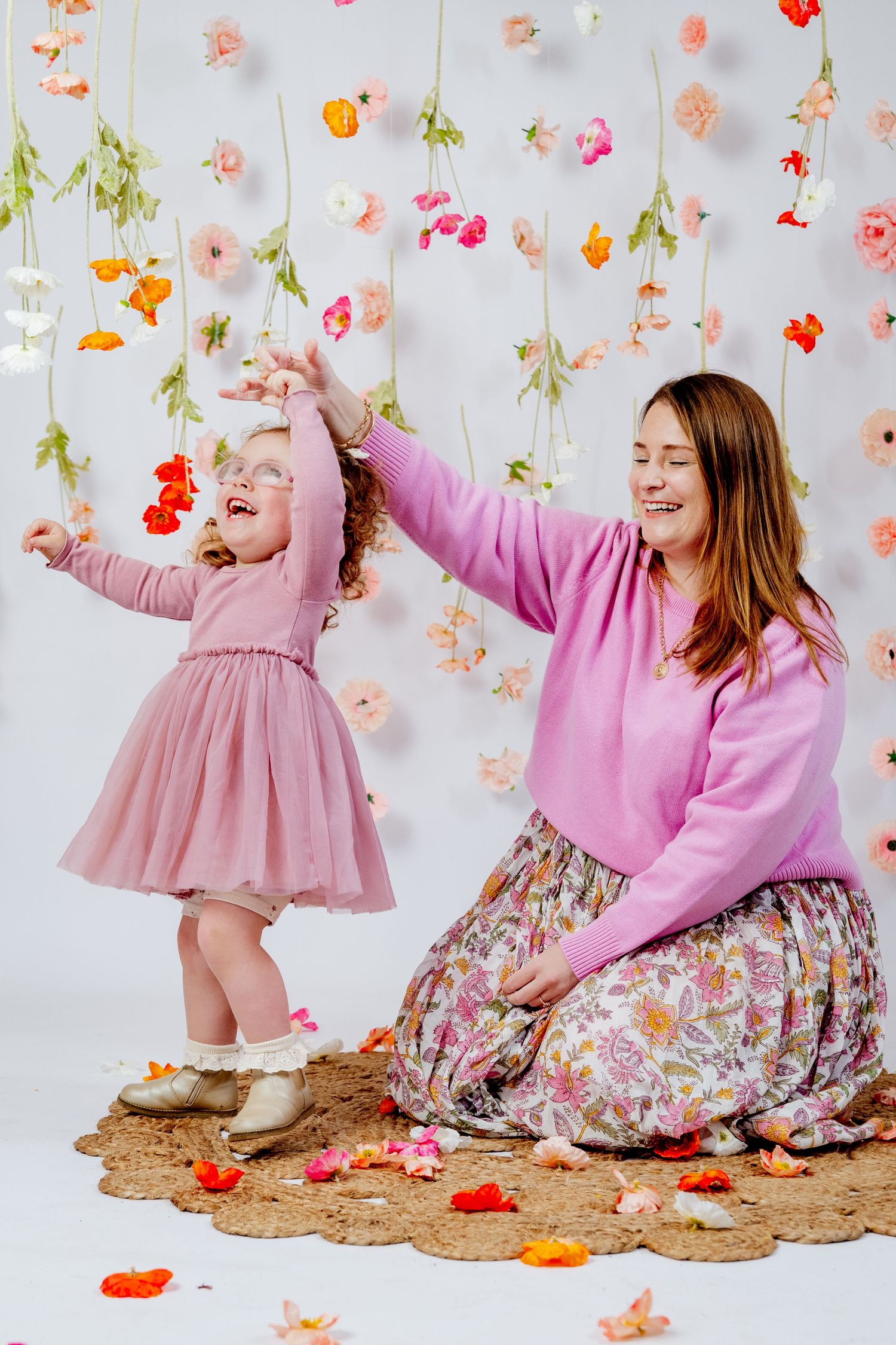 Pregnant woman sitting on floor smiling with toddler girl in pink tutu dress during maternity photo session.