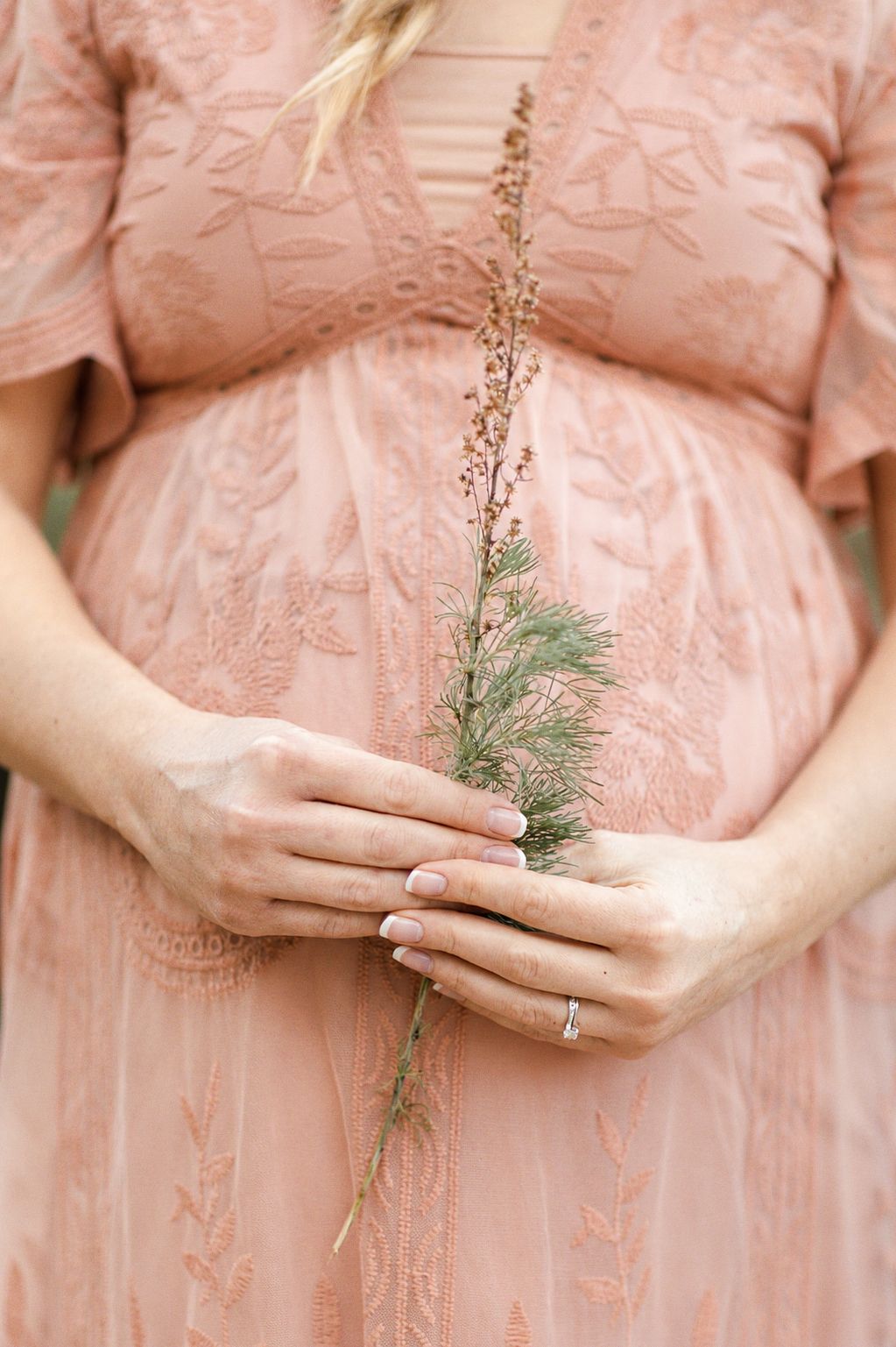 Pregnant couple holding hands on a scenic dirt path surrounded by trees during an outdoor maternity photoshoot.
