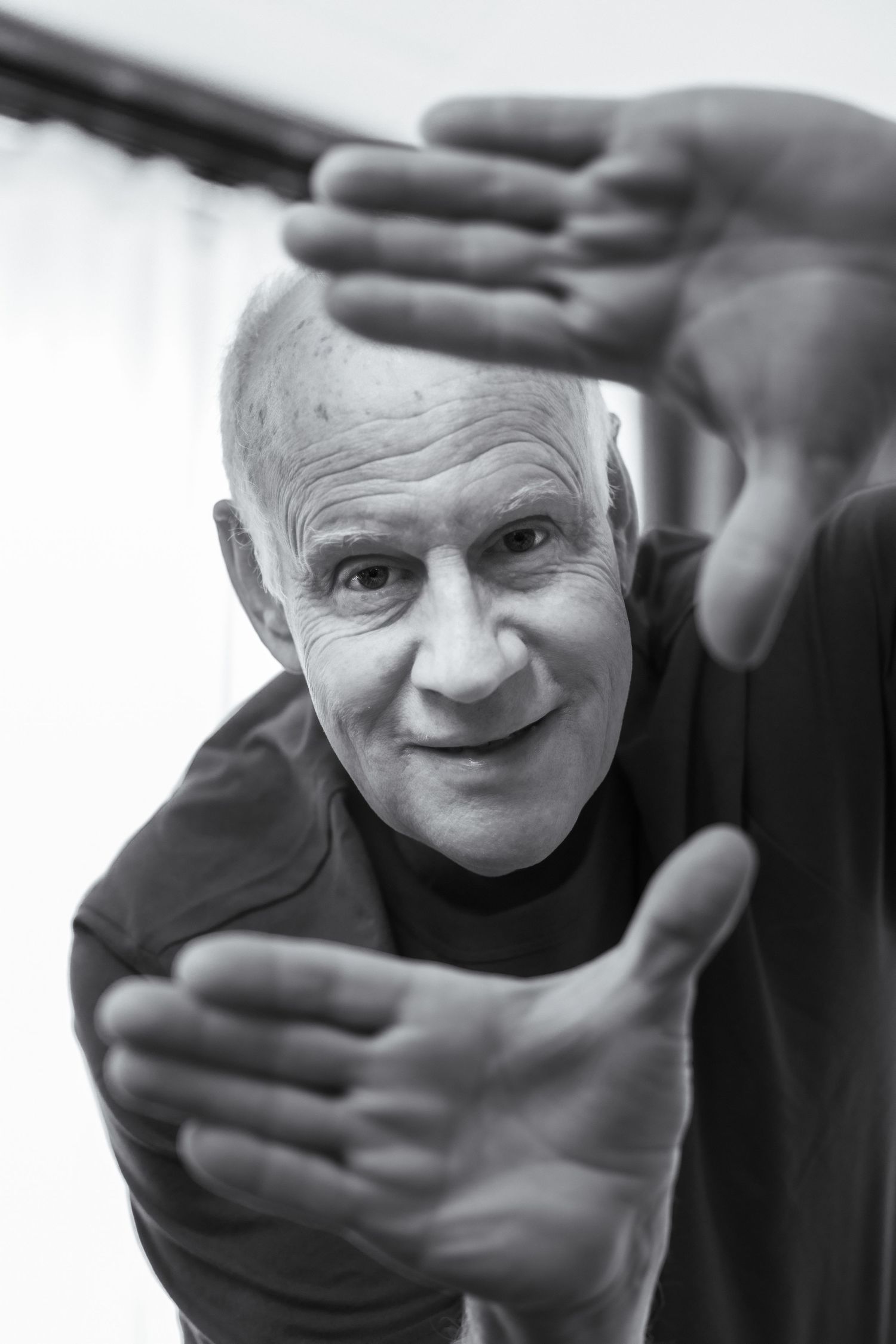 Black and white portrait of smiling senior man framing face with hands, looking at camera.