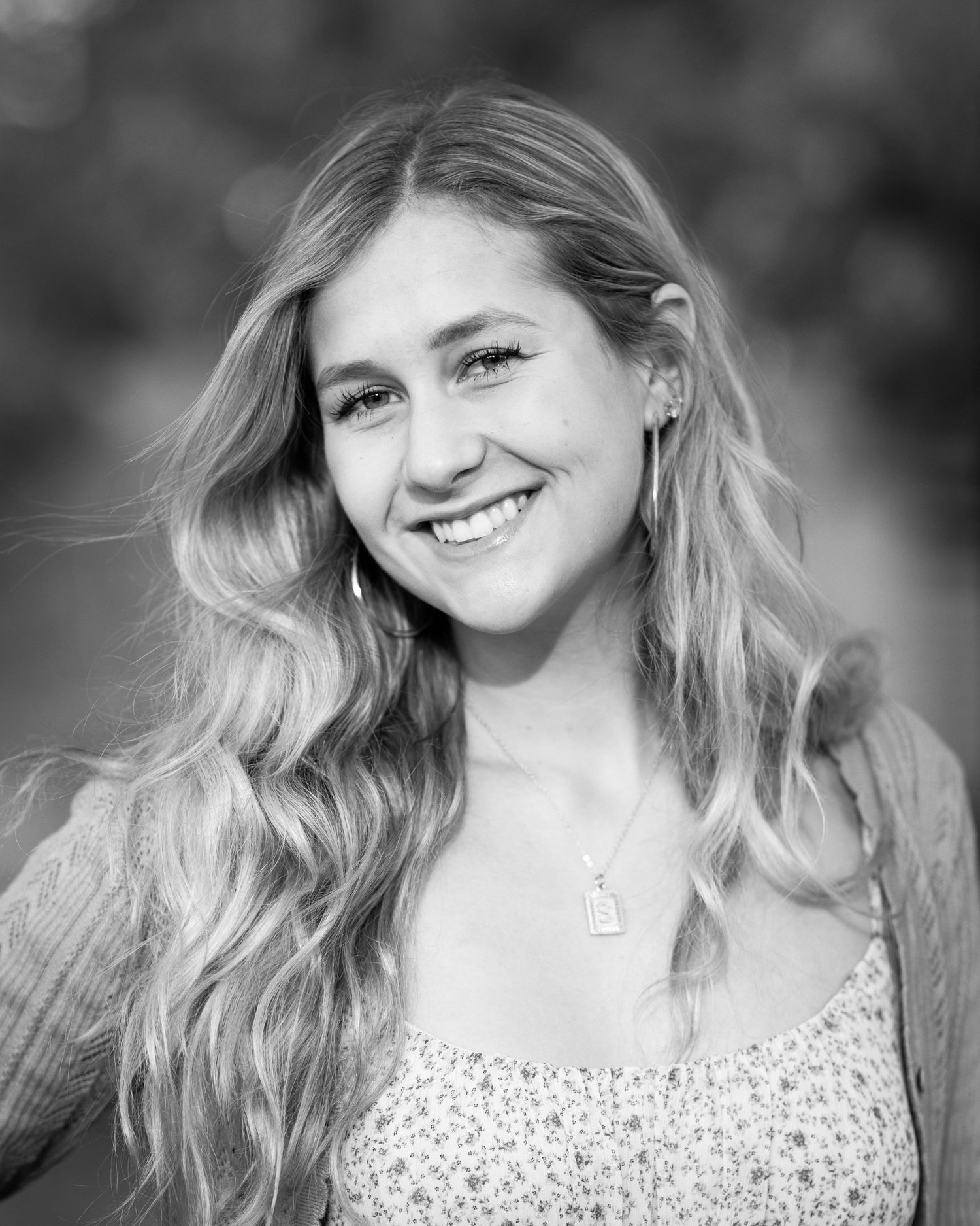 Black and white portrait of a smiling young woman with long wavy blonde hair wearing a floral top and necklace.
