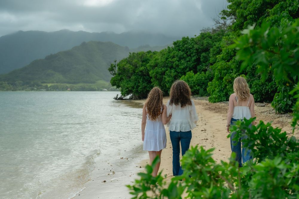 3 women walking on beach with Koolau mountains behind them. Their backs are to the camera.