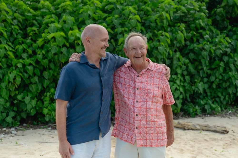 A son and his father laughing on the beach together.