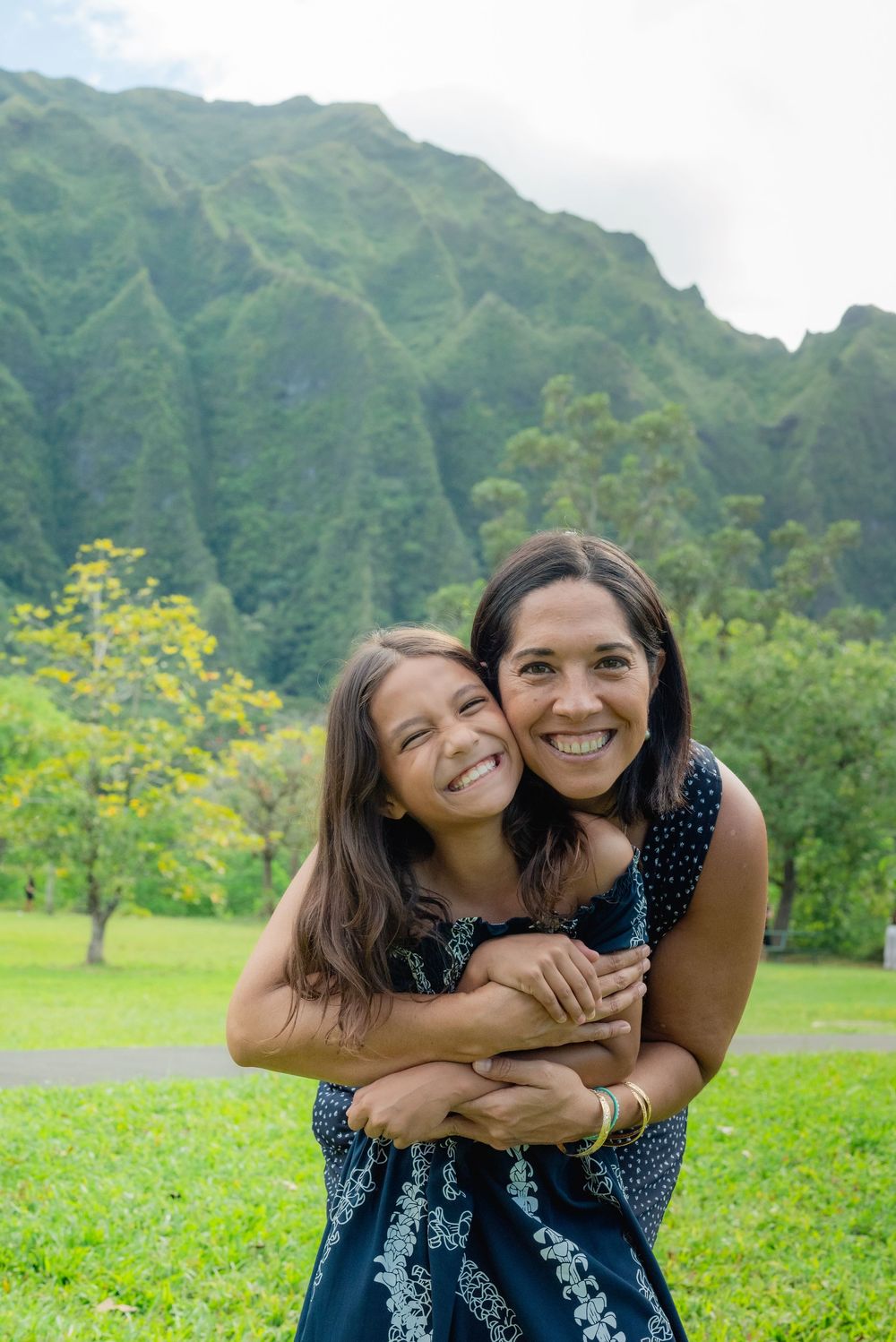 mom and daughter portrait with green hawaii mountains in the background.