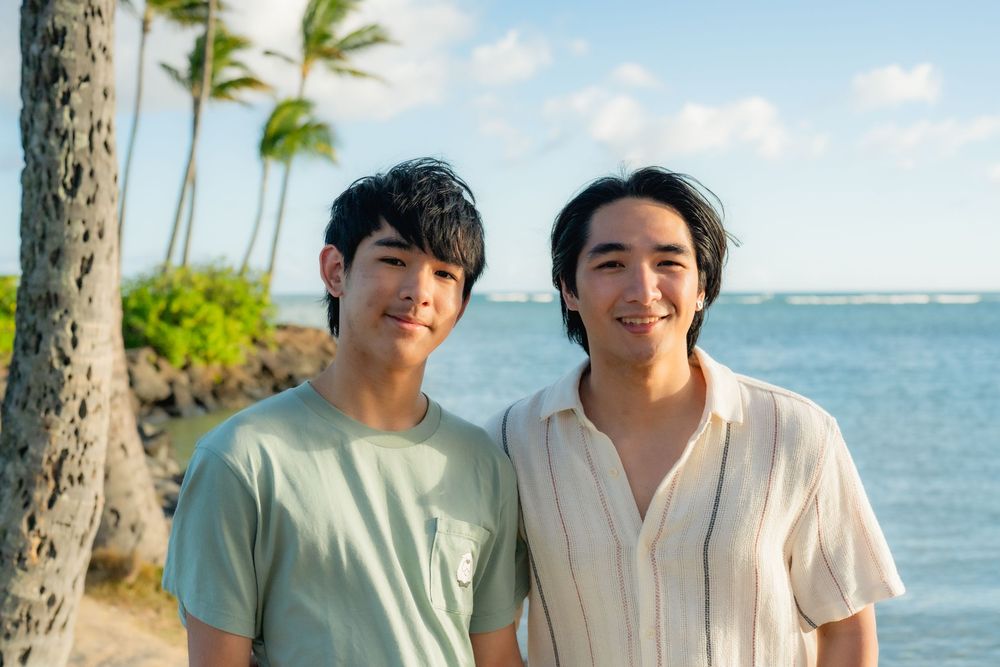 Two brothers smiling at the beach with palm trees.