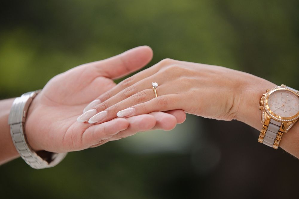 Close-up of a couple's hands touching, woman wearing a diamond engagement ring and gold watch.