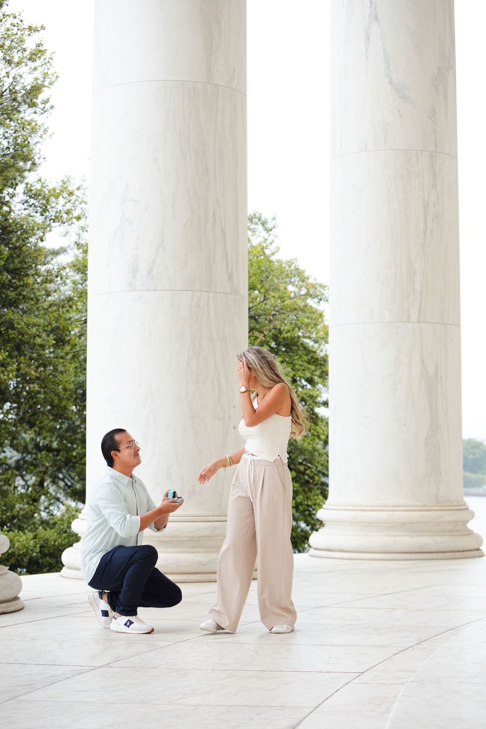 Man proposing marriage on one knee to woman beside marble columns at Jefferson Memorial in Washington DC.