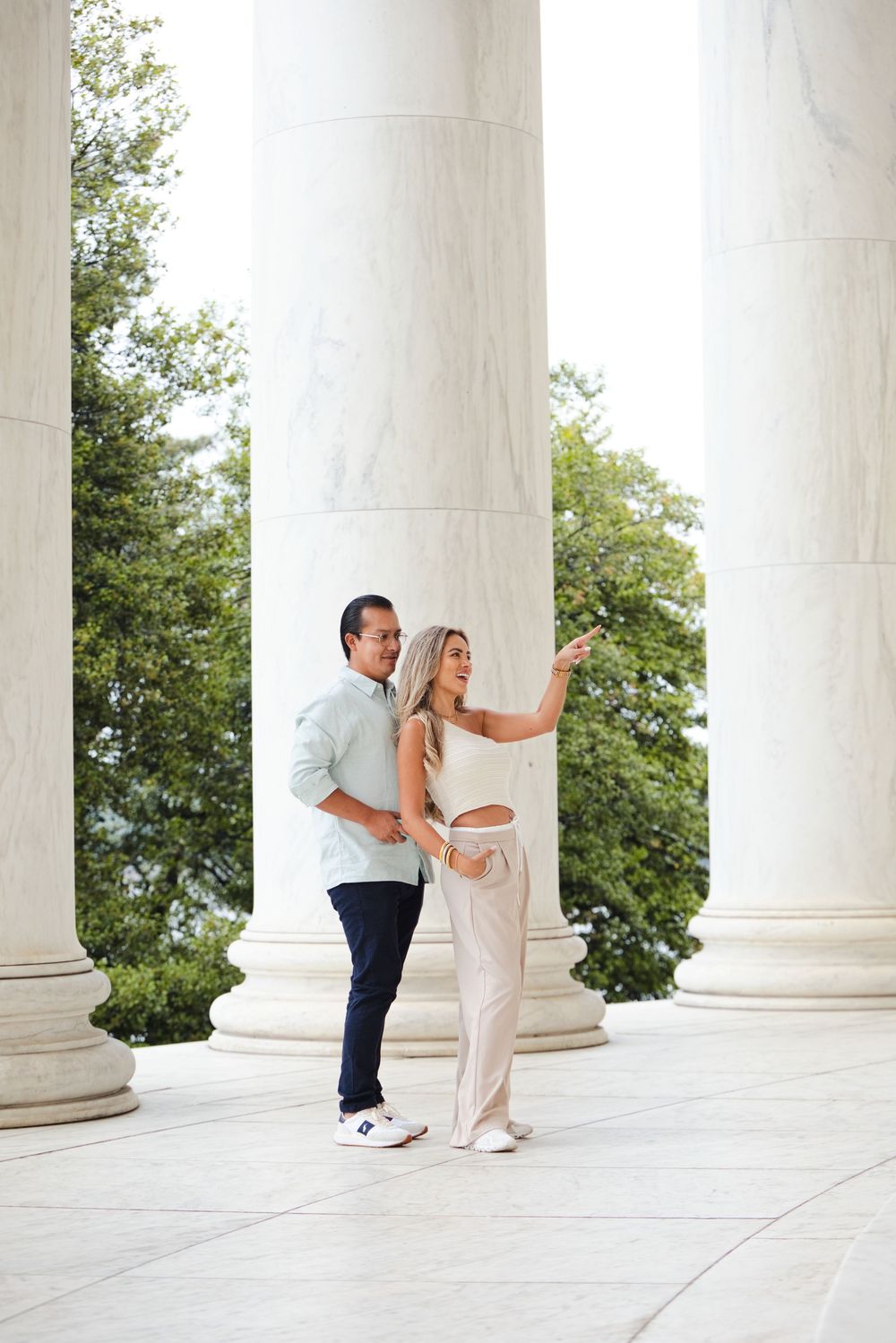Couple posing between white marble columns at the Jefferson Memorial, Washington D.C., on a sunny day.