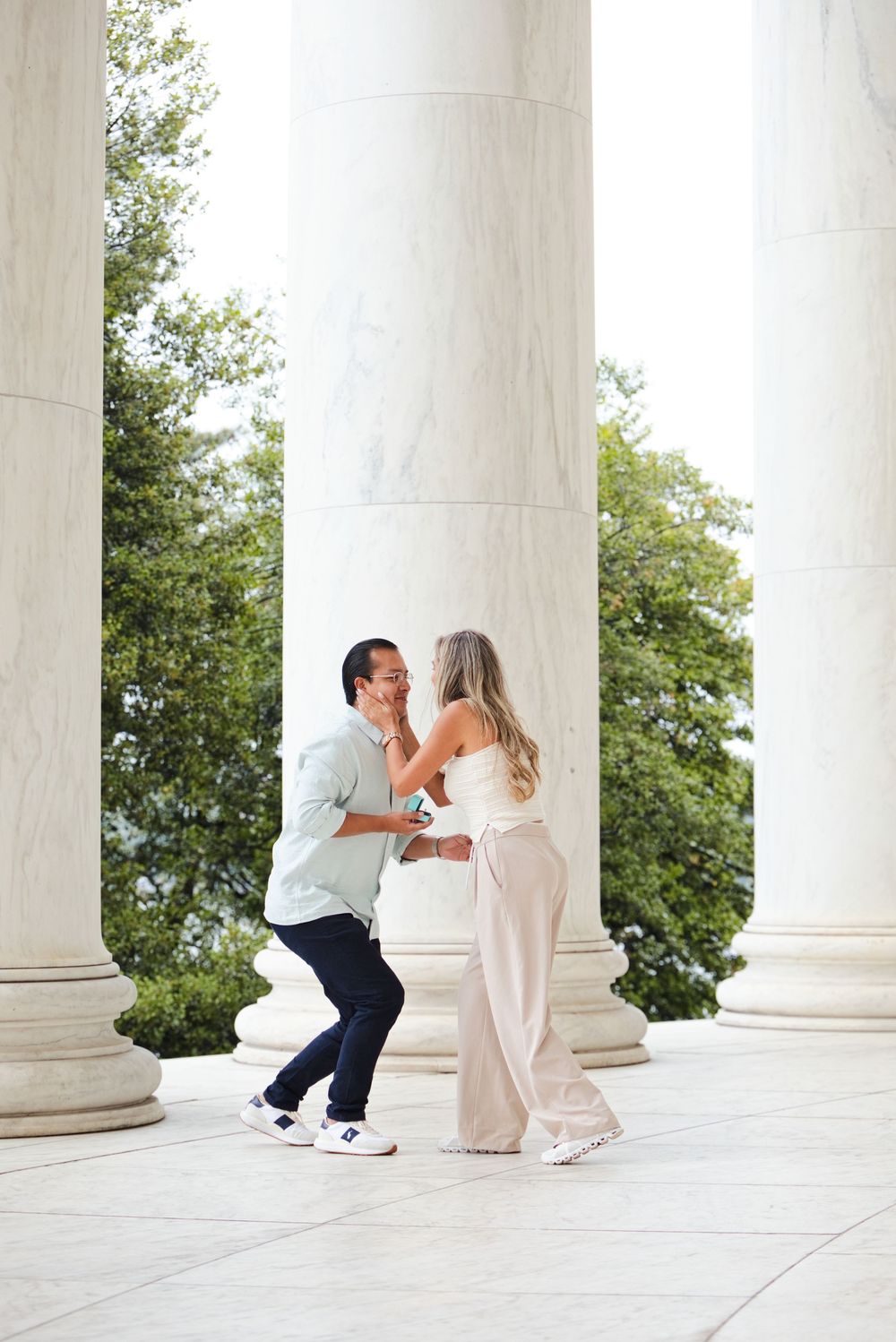 Couple sharing a romantic proposal moment between white marble columns at the Jefferson Memorial.