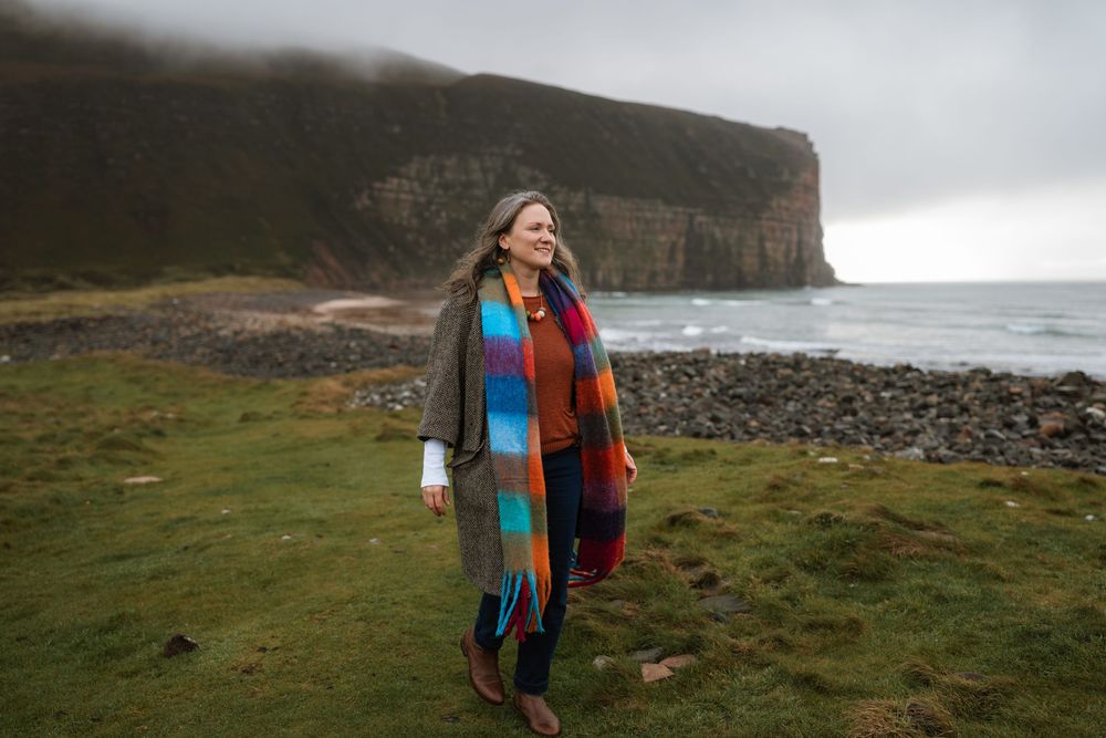 A person in a colorful scarf explores the dramatic coastal cliffs and green landscapes of Ireland on a cloudy day.