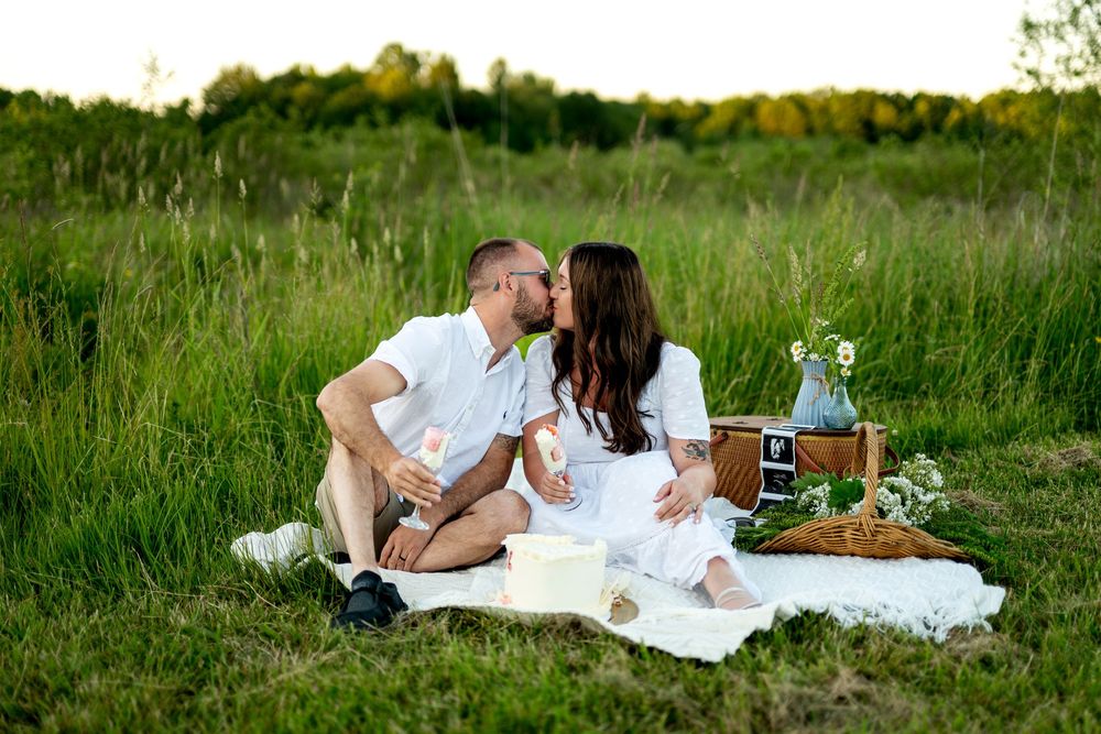 Romantic couple kissing on white blanket during outdoor picnic in a sunny green meadow.