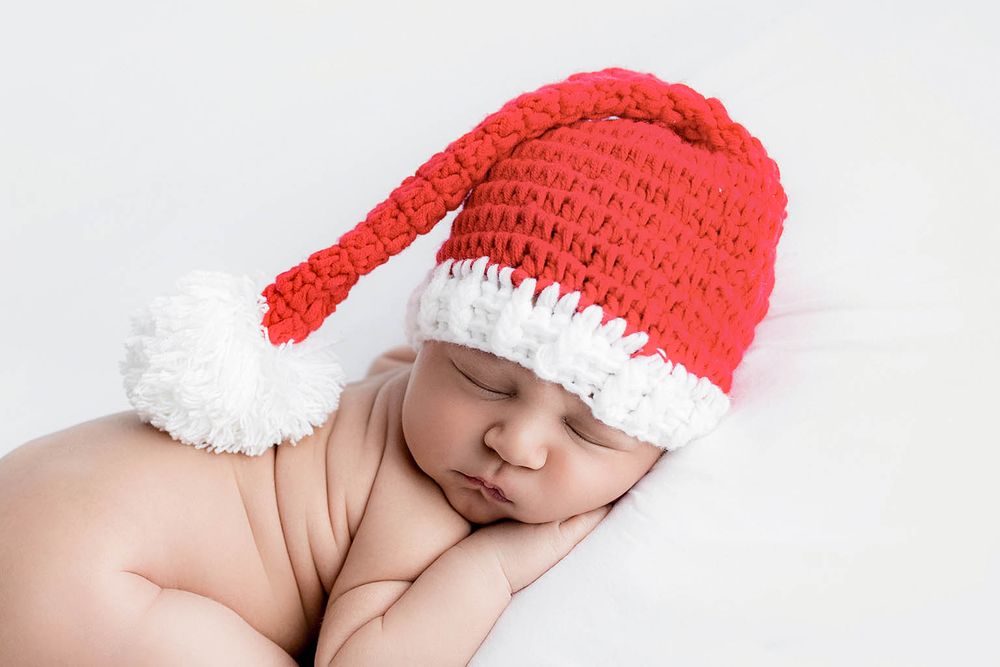 Sleeping newborn baby wearing a red and white crocheted Santa hat on a white background.