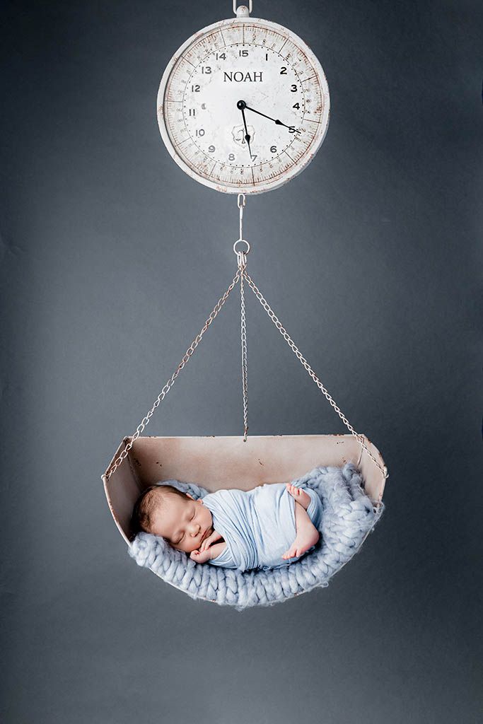 Newborn baby named Noah sleeping peacefully in a vintage scale basket in a studio photo.