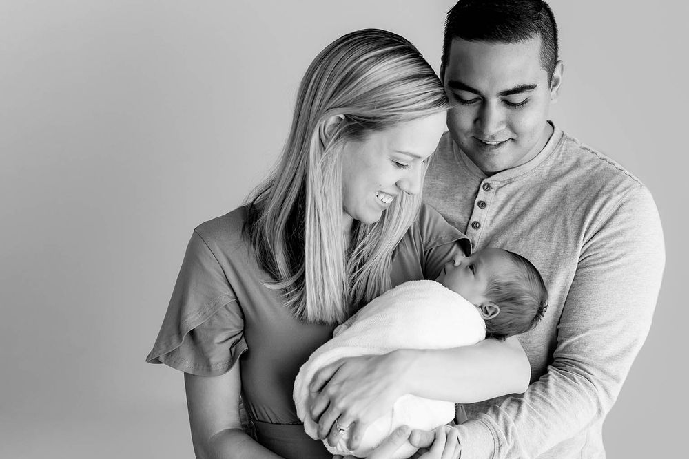 Black and white photo of parents lovingly holding their newborn baby together.